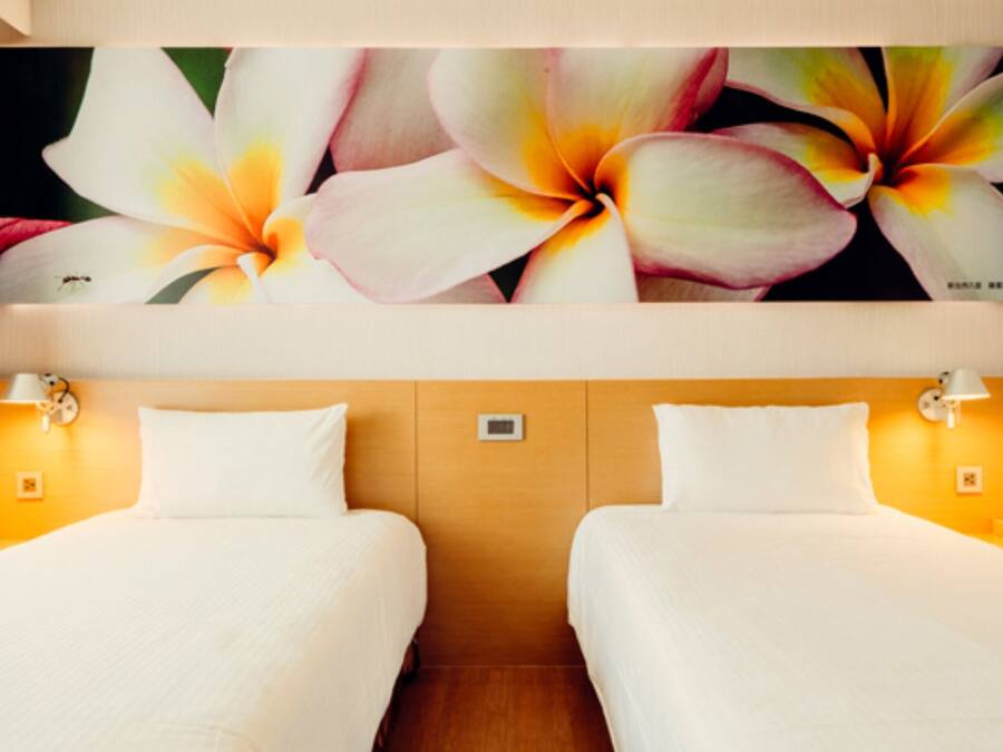 Une chambre d’hôtel avec deux lits, une grande œuvre d’art florale au-dessus des lits et des lampes de chevet.