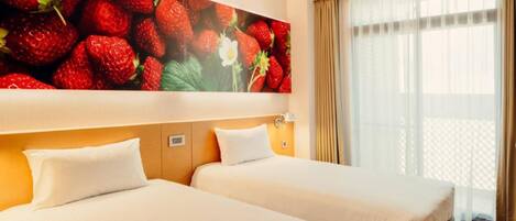 A hotel room with two beds, a large wall mural of strawberries, a window with curtains, and a visible thermostat.