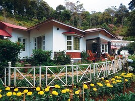 A white building with a red roof, surrounded by a white fence and a garden with yellow flowers.