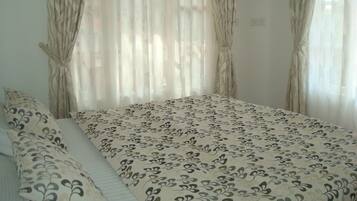 Un dormitorio con cama, dos almohadas y cortinas translúcidas.