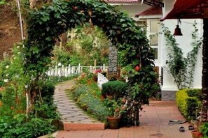 A garden pathway with a stone-tiled path leading through a lush, vine-covered archway.