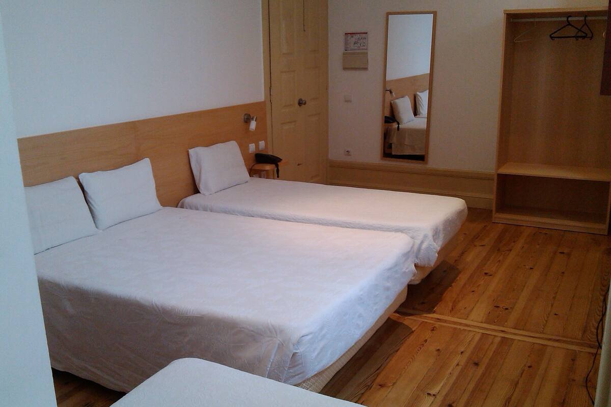A room with two single beds, a wooden wardrobe, a mirror, and a small table.
