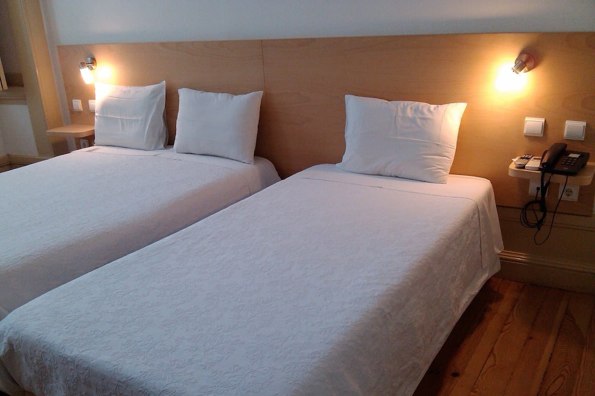 A hotel room with two beds, wooden headboard, bedside lamps, a phone, and a small table.