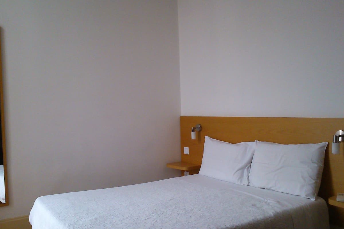 A hotel room with a bed, a nightstand, a mirror, and a wooden headboard.