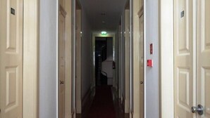 Un couloir d’hôtel avec un tapis rouge, des murs blancs et des portes de chaque côté.