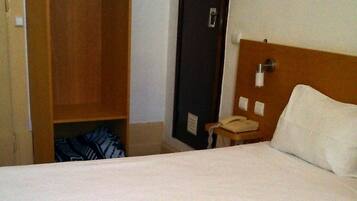 A hotel room with a bed, a wooden wardrobe, a bedside table with a phone, and a door.