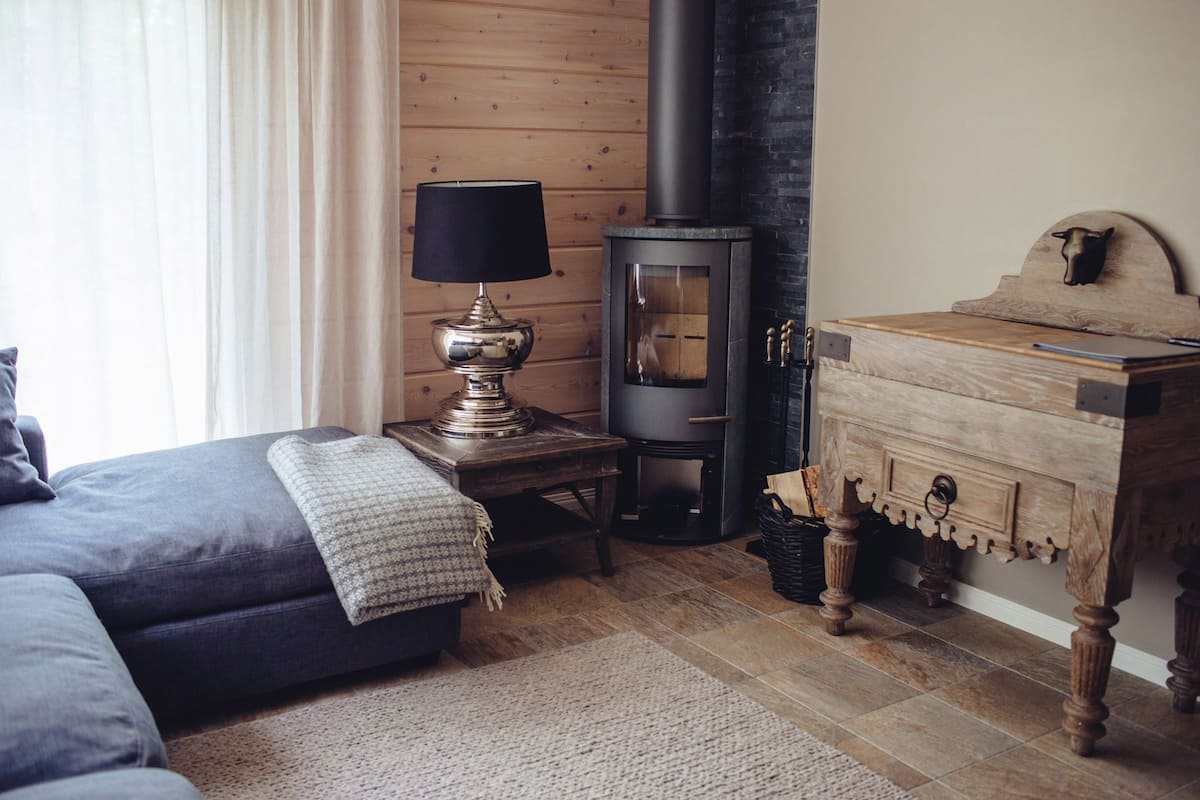 Um quarto aconchegante com sofá, luminária, cômoda de madeira e lareira a lenha.