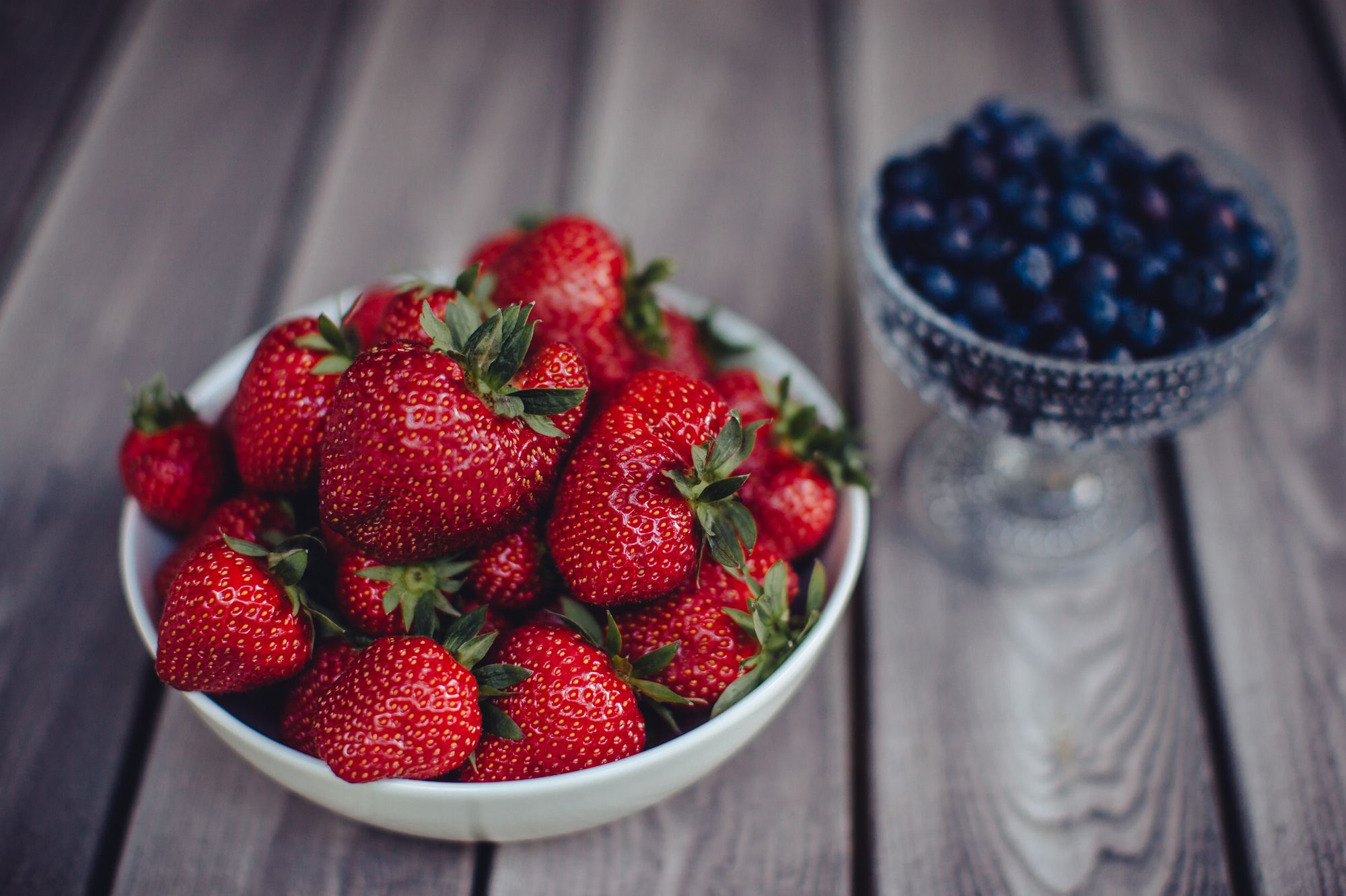 Eine Schale Erdbeeren und eine Schale Blaubeeren auf einer Holzoberfläche.