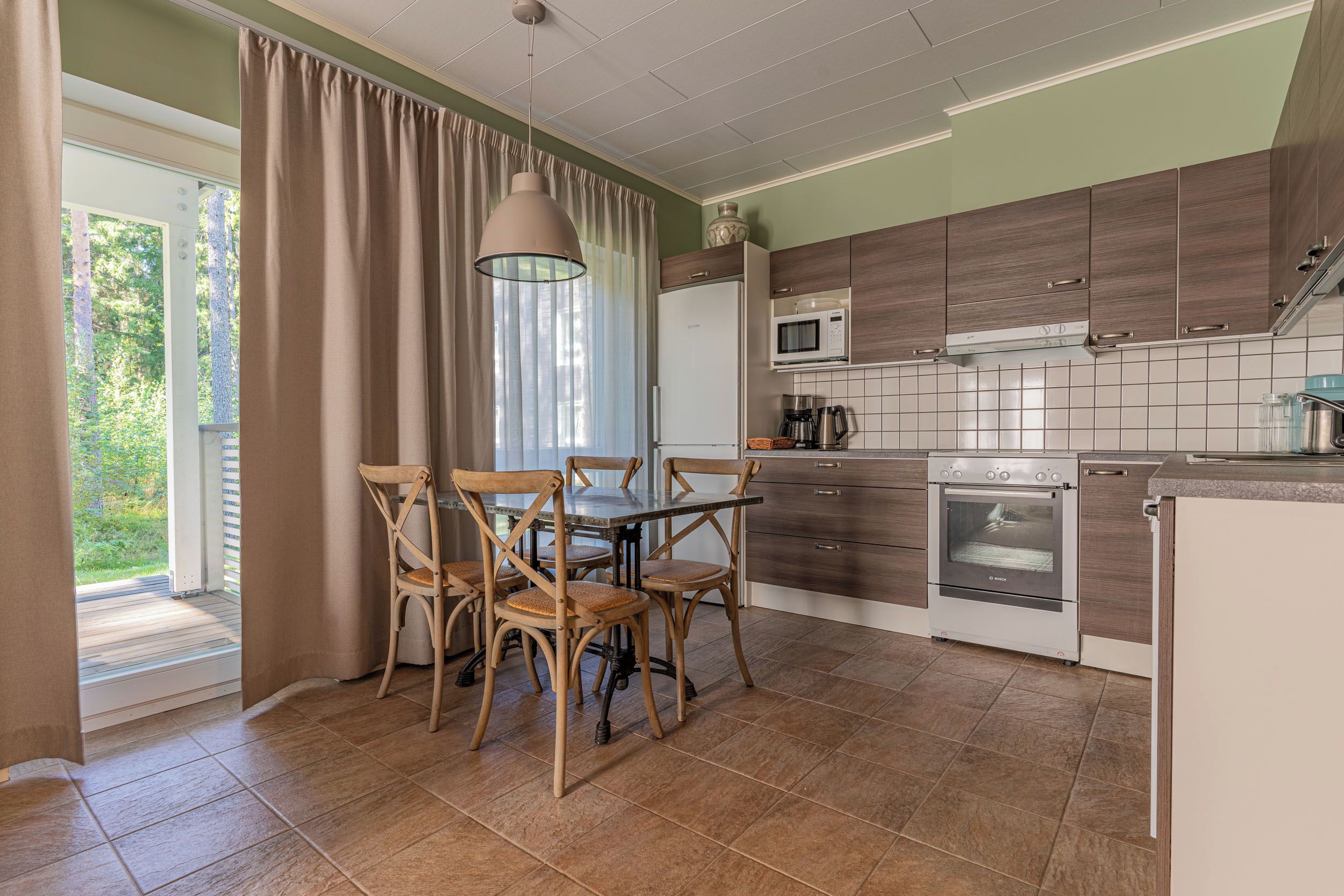 Une cuisine équipée d’une table à manger, de chaises, d’un four à micro-ondes, d’une cuisinière et offrant une vue sur la verdure environnante.