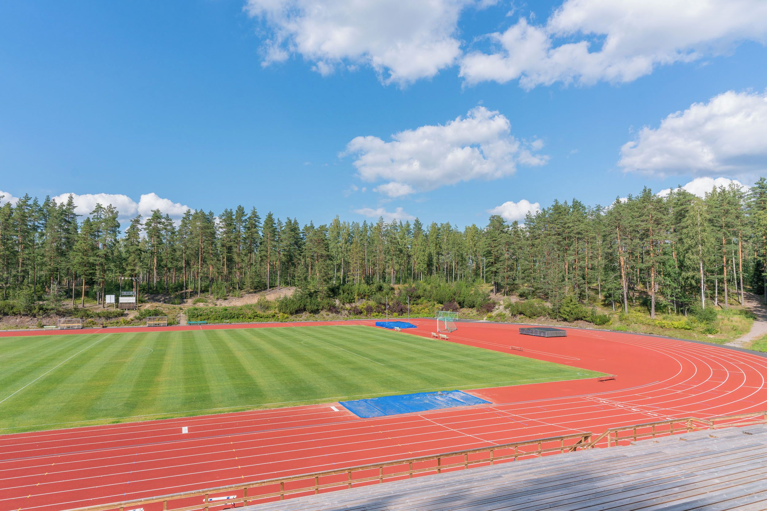 A sports track with a surrounding grassy area and a forest backdrop.