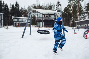 Een kind speelt op een schommel in een besneeuwd landschap, met een modern huis op de achtergrond.