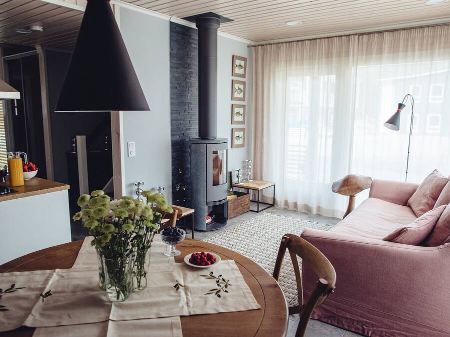 A cozy living room with a pink sofa, a round wooden table with a vase of flowers, and a modern fireplace.