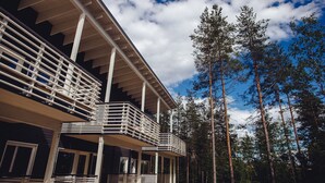 A multi-story building with balconies and a forested background.