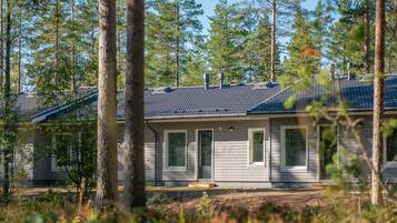 A single-story cabin with a dark roof, surrounded by tall pine trees.