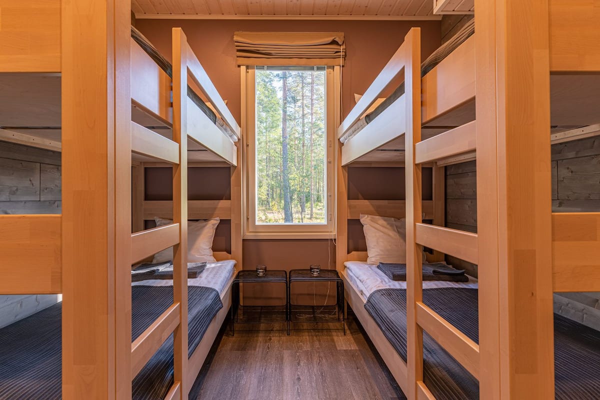 Quarto compacto com beliches, uma mesinha e janela com vista para a floresta.