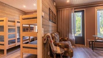 Interior acogedor de una cabaña con literas de madera, una zona de estar con cojines y una mesa de comedor.