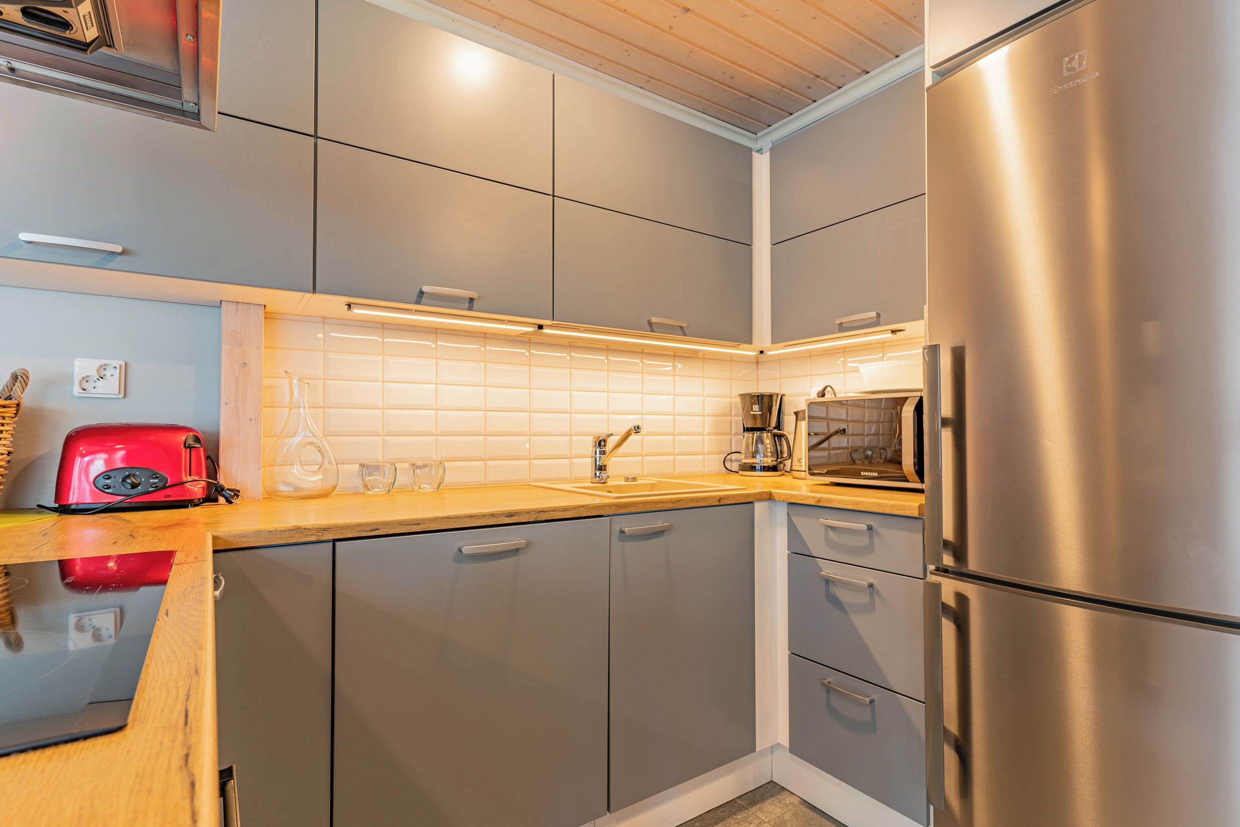Een moderne keuken met grijze kastjes, roestvrijstalen apparatuur en een houten aanrecht.