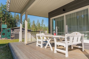 Eine Holzterrasse mit Tisch und Stühlen, einer Spielanlage und einem großen Fenster.