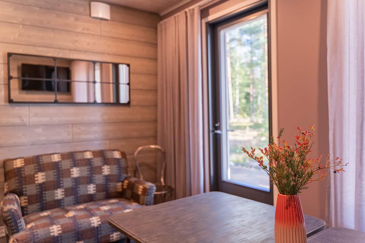 Um quarto aconchegante com parede de madeira, sofá estampado, uma mesa e janela com cortinas.