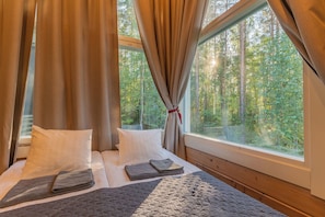 A bedroom with a large window, a bed with pillows and a blanket, and curtains.