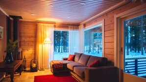 A cozy living room with a wooden interior, a red rug, and a large window offering a view of a snowy landscape.