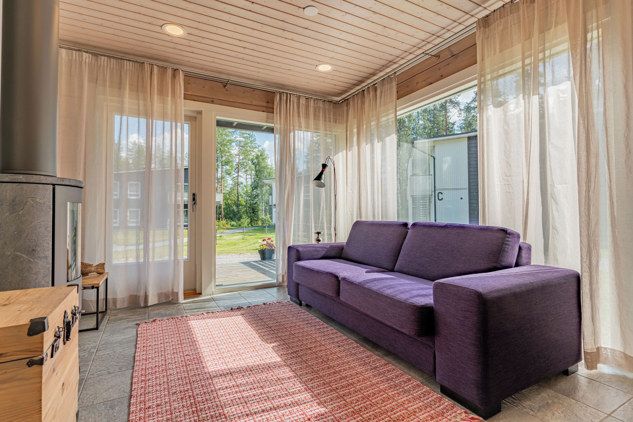 A modern living room with a purple sofa, a wooden cabinet, and a large window with sheer curtains.