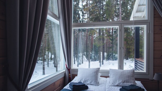 A bed with white and blue bedding, a window with a view of a snowy forest, and wooden walls.