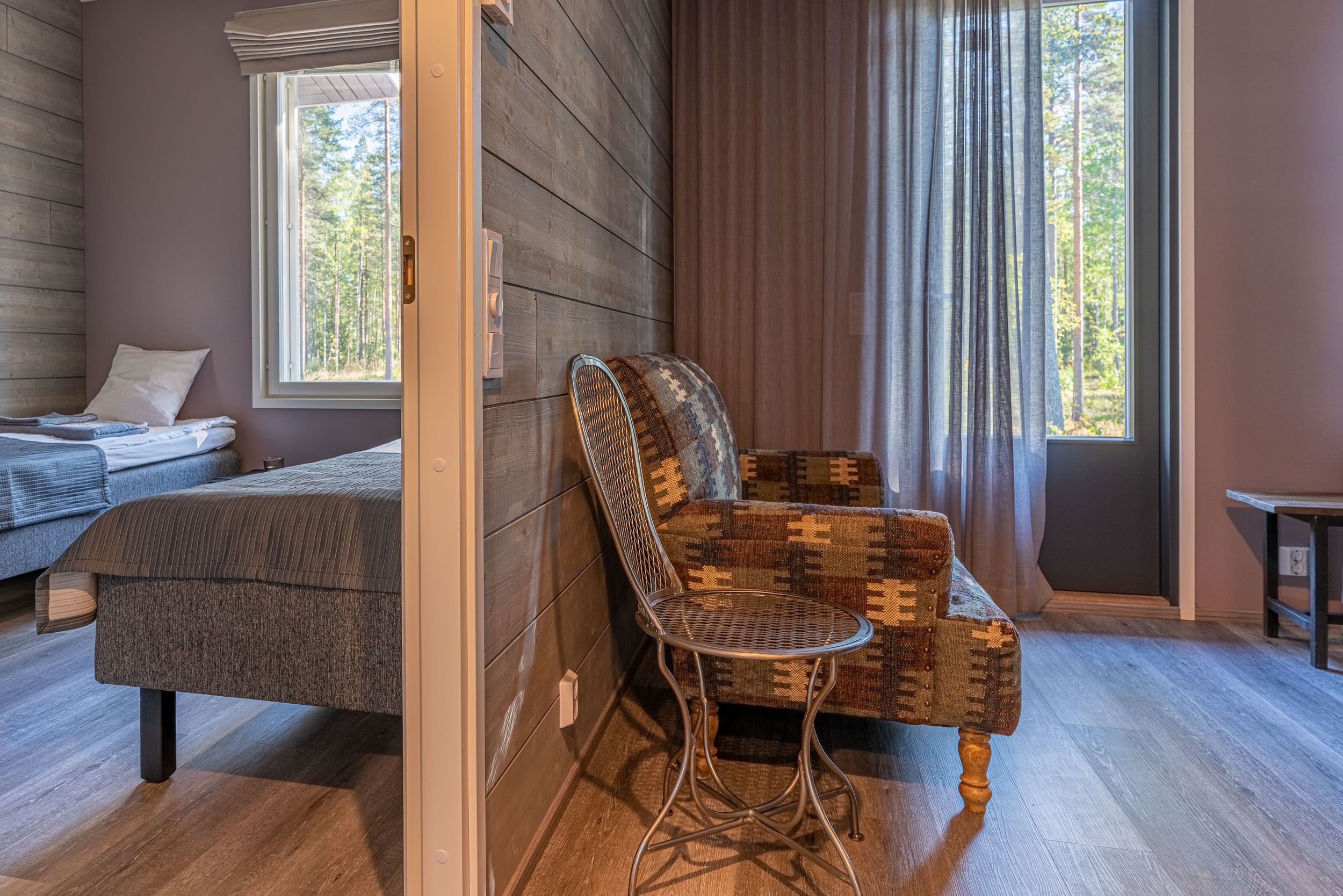 Una habitación acogedora con una cama, un sillón estampado y una ventana con cortinas.