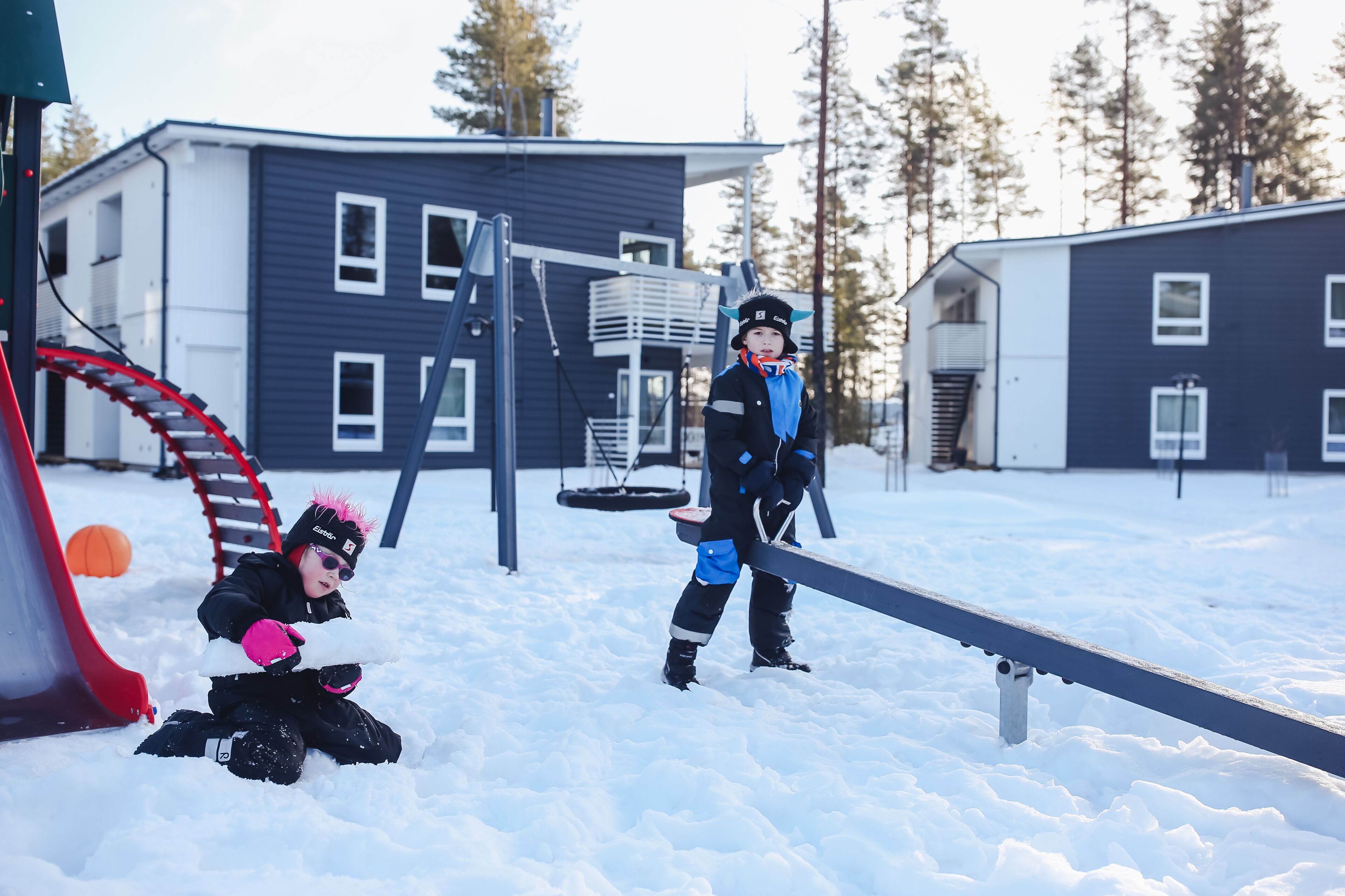 Un parque infantil con un tobogán rojo y un sube y baja en un área exterior nevada.