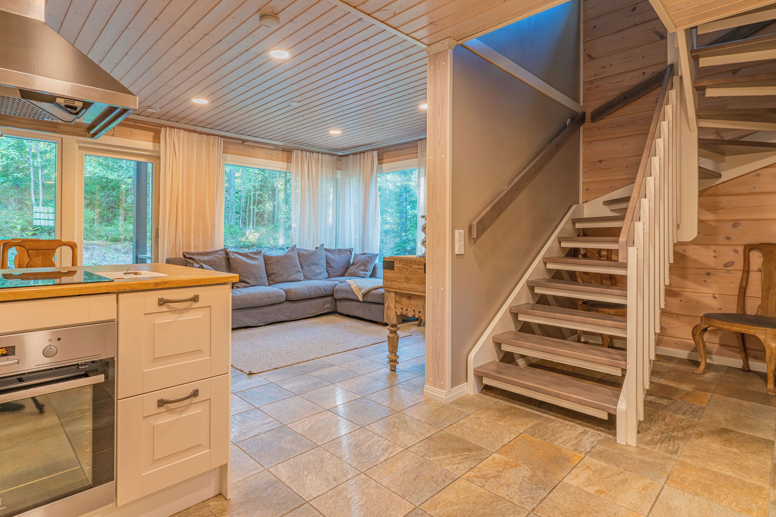 A modern kitchen with a built-in oven, a dining area with a wooden table, and a staircase leading to an upper level.