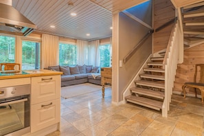 A modern kitchen with a built-in oven, a dining area with a wooden table, and a staircase leading to an upper level.