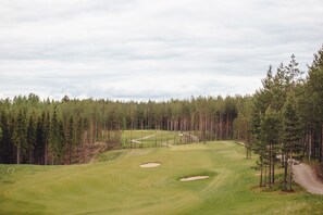 Een golfbaan met een duidelijke route, zandbunkers en een dicht bos op de achtergrond.