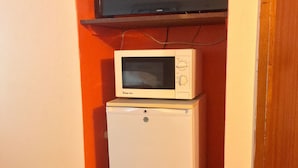 A compact refrigerator and microwave unit placed in a corner of a room with wooden flooring and a red wall. - Monique's Guesthouse (Port of Spain)