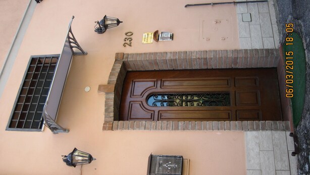 Facciata di un edificio con una porta numerata, una finestra con inferriata e due lampioni a parete.