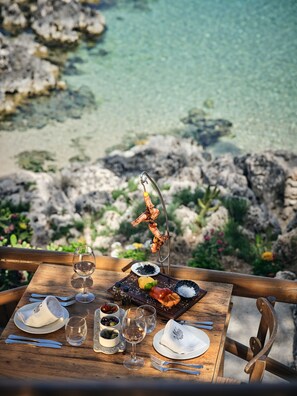 A table set for a meal with seafood, wine, and a view of a rocky coastline.