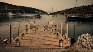 A wooden dock with two chairs and lanterns, leading to calm water with boats and a hilly landscape in the background. - Nobelos Seaside Lodge (Zakynthos)