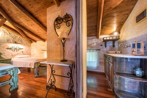 A rustic wooden interior with a bed, a table with a lamp, and a kitchen area with a sink and cabinets.