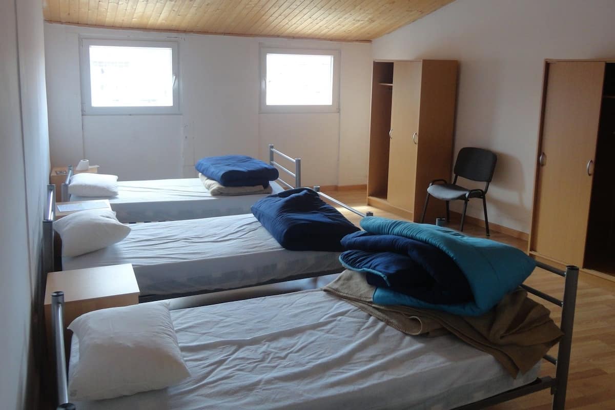 A dormitory room with three single beds, a chair, and a wardrobe.