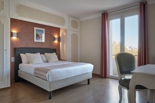 Un dormitorio con una cama grande, un escritorio y una silla. Hay una ventana con cortinas, un muro de ladrillo y un cuadro en la pared.