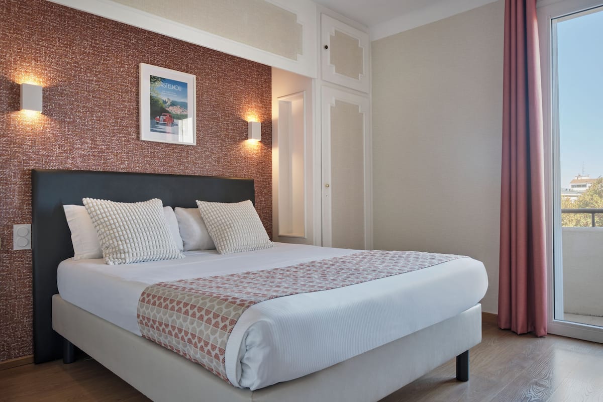 Habitación de hotel con una cama grande, pared de ladrillo decorativa, un cuadro enmarcado y vistas al exterior.