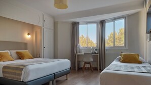 A bedroom with two beds, a desk, and a window with a view of trees. - The Originals City, Hôtel Mondial, Perpignan (Perpignan)