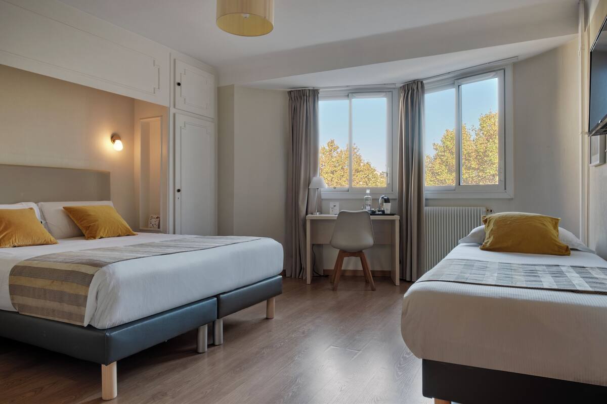 Un dormitorio con dos camas, un escritorio y una ventana con vistas a árboles.