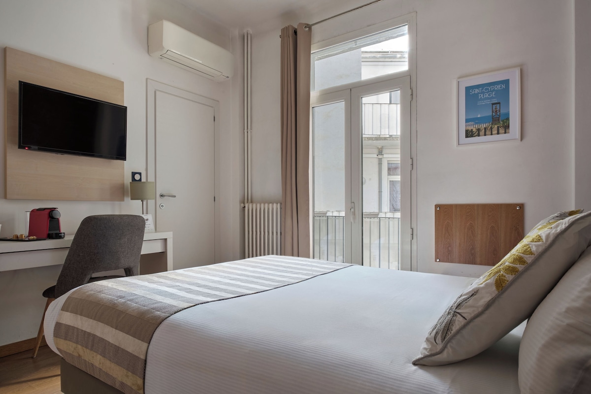 A hotel room with a bed, a desk, a chair, a TV, and a window with curtains.