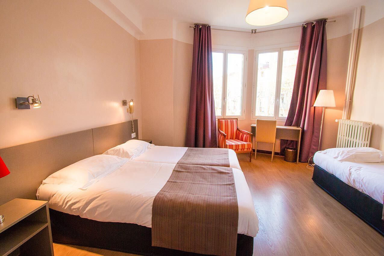 Een hotelkamer met twee bedden, een bureau, een stoel en een raam met gordijnen.