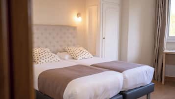 Habitación doble con dos camas, cada una con cabecera y almohadas. Incluye mesitas de noche y una ventana con cortinas.