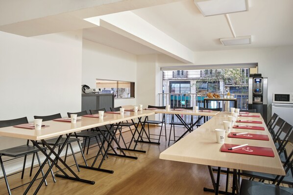 A conference room with long tables, chairs, and a kitchenette area. - The Originals City, Hôtel Mondial, Perpignan (Perpignan)