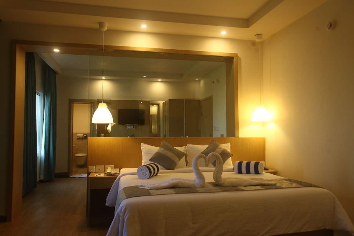 A hotel room with a bed, a nightstand, a mirror, and a bathroom visible through an open door.