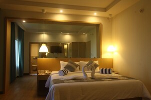Habitación de hotel con cama, mesita de noche, espejo y baño visible a través de una puerta abierta.