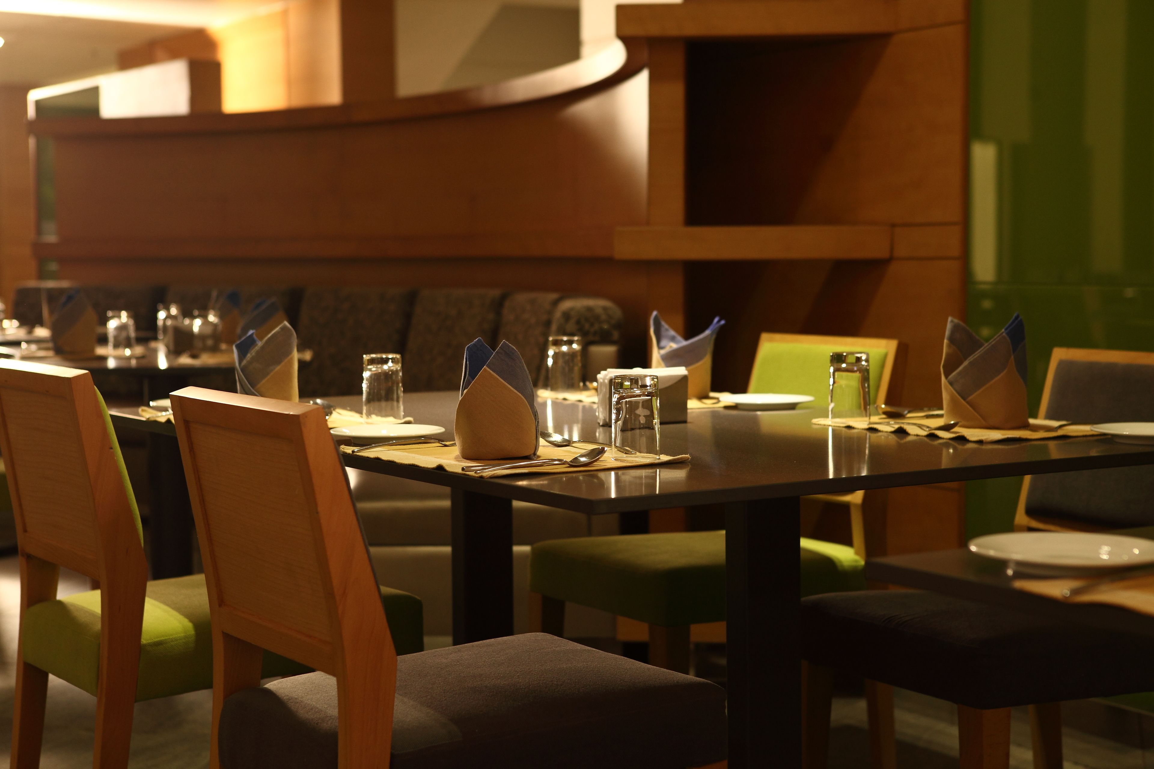 A dining area with wooden chairs and tables, each set with plates, cutlery, and glasses.
