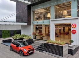 A modern building with a glass facade, a red car parked in front, and a logo on the right side.
